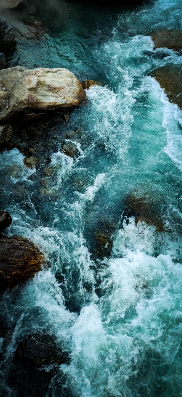 A vibrant aerial shot of a turquoise river rushing through rocky terrain in India.